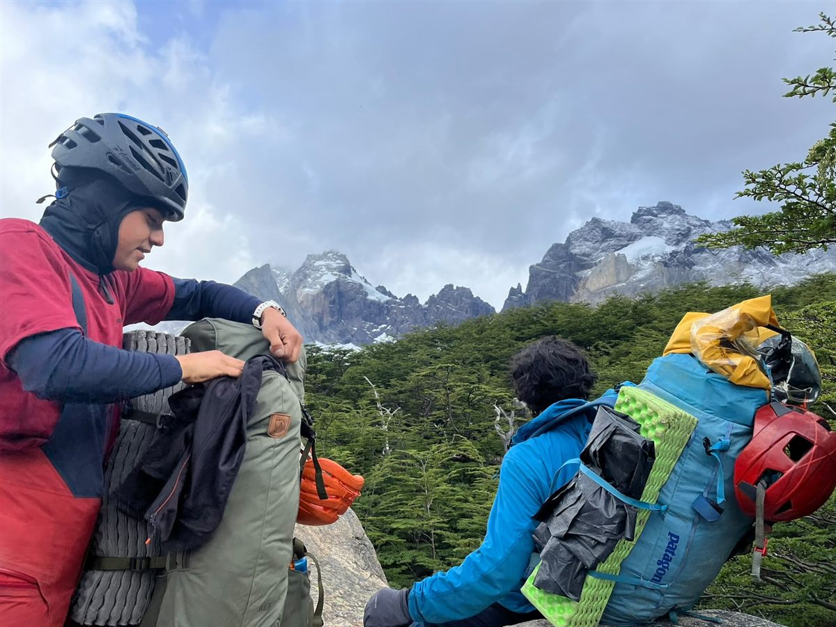 Dos escaladores preparando equipo en el bosque frente a los Cuernos del Paine