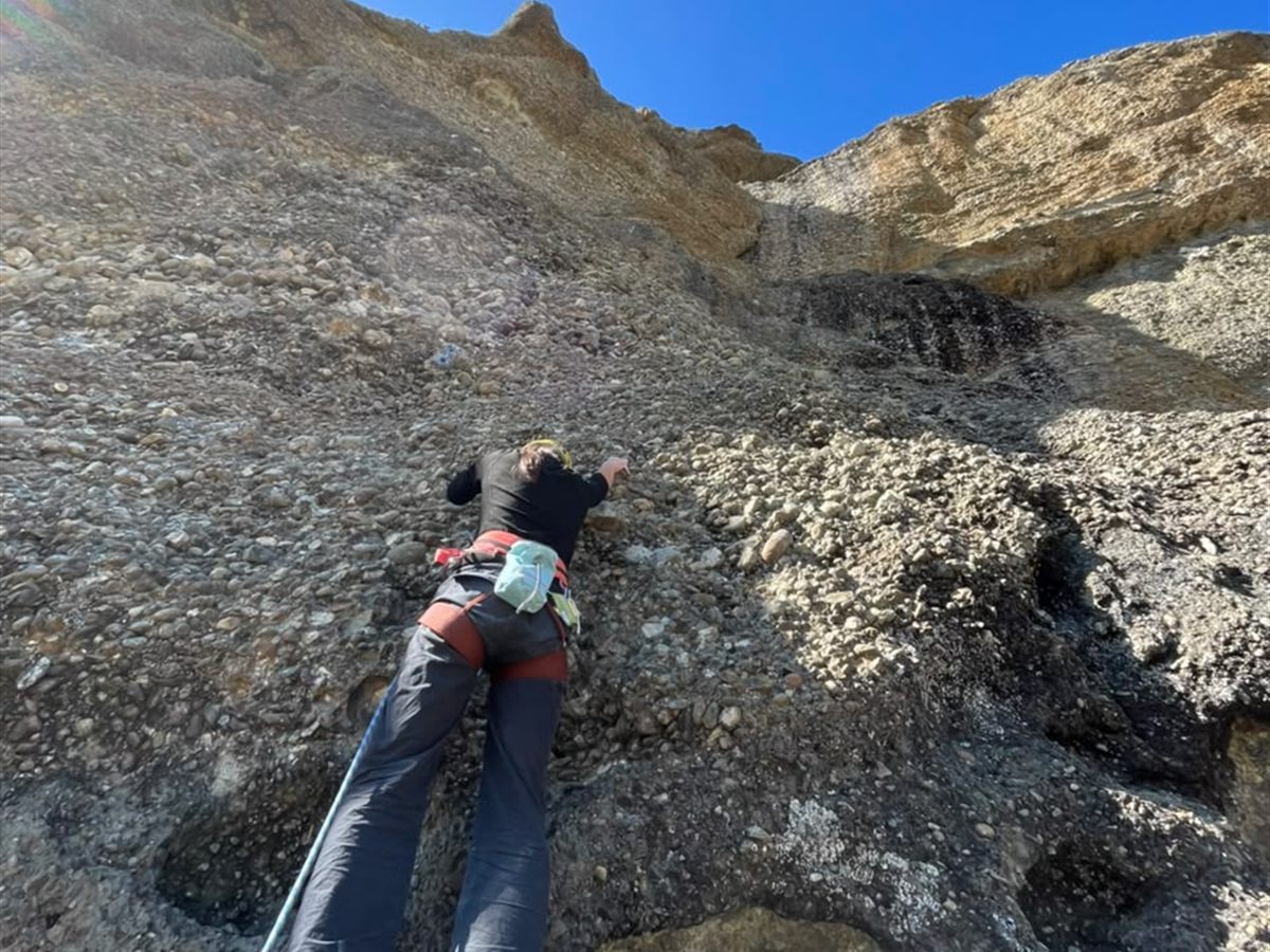 Escaladora progresando en pared de conglomerado bajo cielo despejado, Laguna Sofía