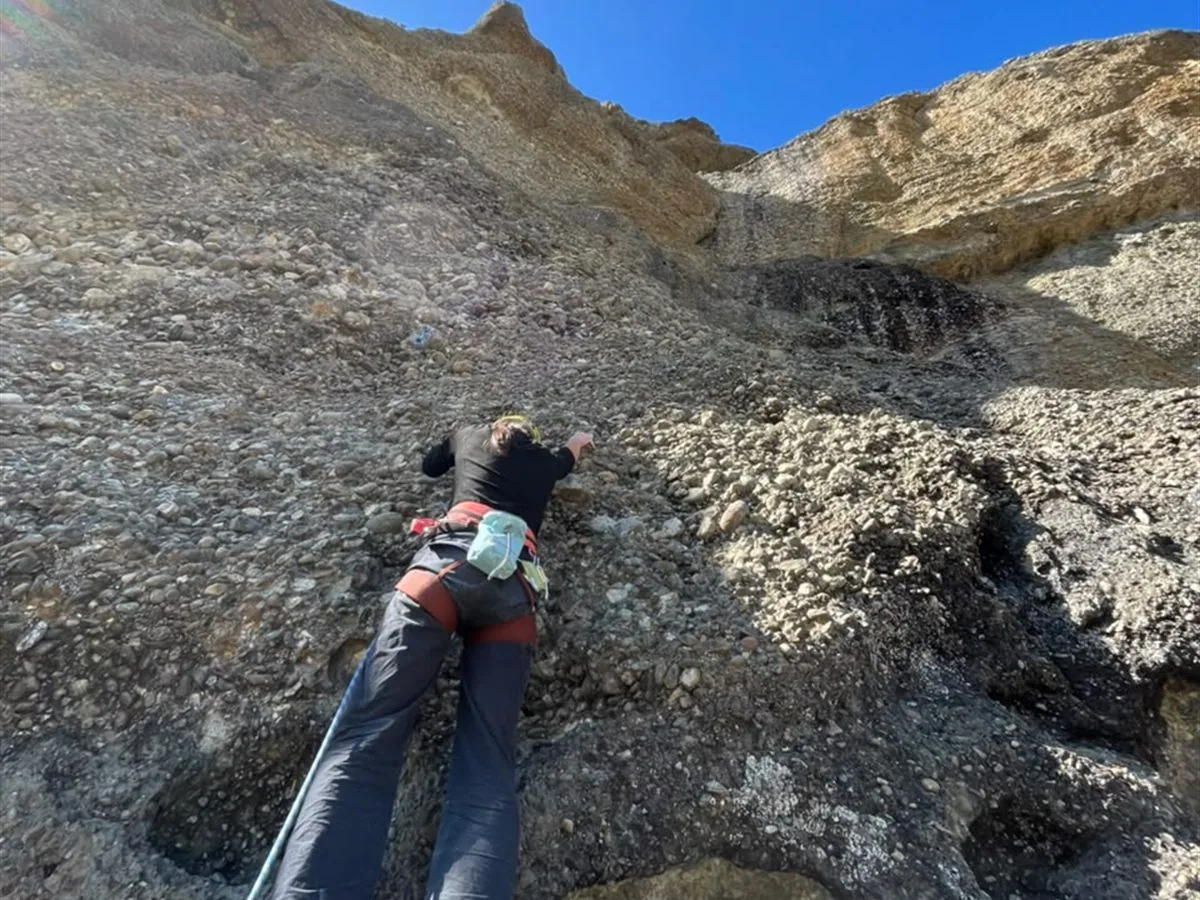 Escaladora progresando en pared de conglomerado bajo cielo despejado, Laguna Sofía