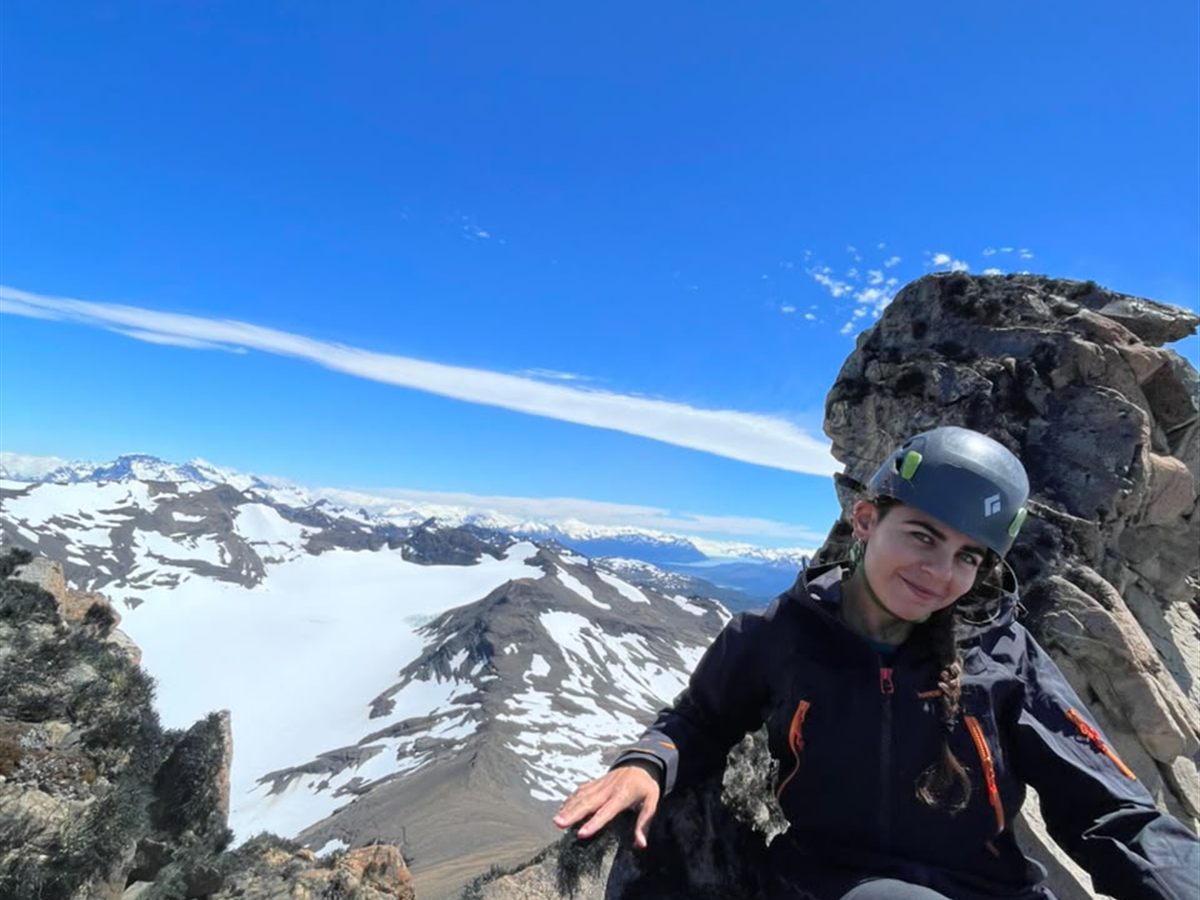 Escaladora en la cumbre con campos de hielo y cordillera nevada al fondo, Patagonia